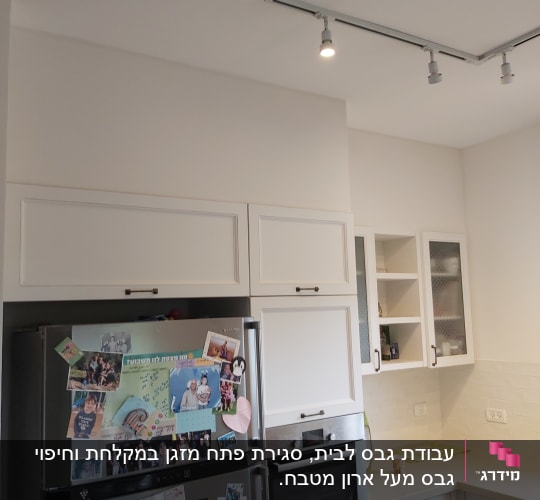 מטבח עם ארונות לבנים ותאורה עליונה